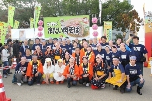 屋外の会場でかほく冷たい肉そば研究会の皆さんが集合している記念写真