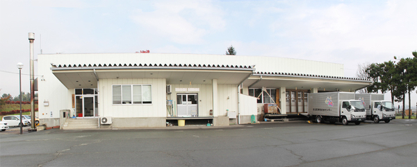 1階建ての白い建物の右端にトラックが2台留まっている学校給食センターの写真