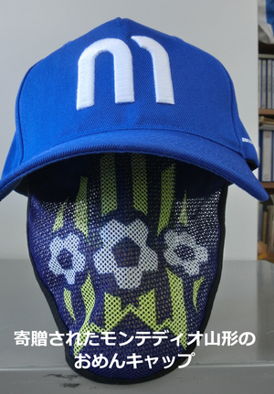 青地に白色でMと刺繍が施された帽子と「寄贈されたモンテディオ山形のおめんキャップ」という文字がはいった写真
