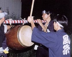 棒に吊るされて担がれている和太鼓を叩いている法被姿の男性の写真