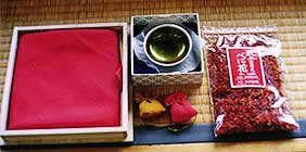 袋に詰められた紅花の花と、黄色と赤の巾着と、木枠に入っている赤い布などの道具一式の写真