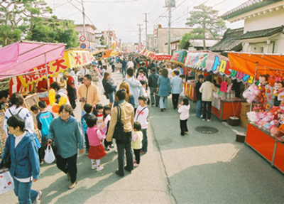 左右に屋台が立ち並んでいるひな市を楽しんでいる町民のみなさんの写真