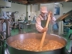 エプロンを着用した人が大きい鍋を棒でかき混ぜ調理している写真