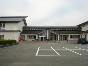 手前に駐車場があり横に広く窓が多い建物の写真