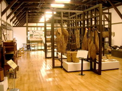 屋内で片方の壁に農具が立てかけられており中心に網目上の木の収納具があり農作業道具が収納されている写真