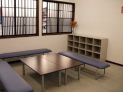 2つ並べた茶色い机とその机を囲うように暗い紫色の椅子が3つ置いてあるクラブルームの写真
