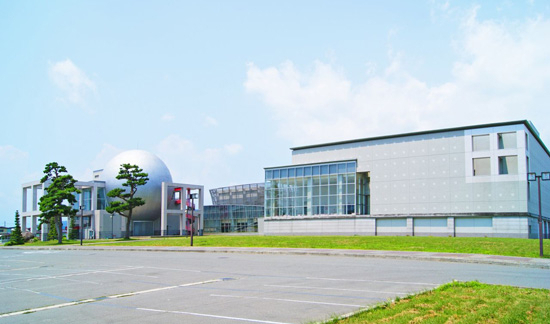 外壁の白い大きな建物と球体のデザインのある建物（サハトべに花）が隣接している写真