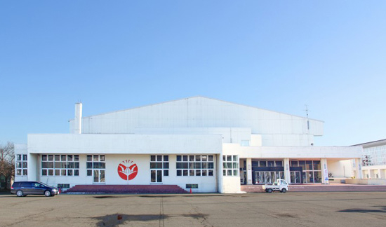 白い壁に赤いシンボルマークが描かれている窓の多い体育館の写真
