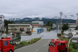 住宅街の道路が地面が見えないほど浸水しており消防車が出動している写真