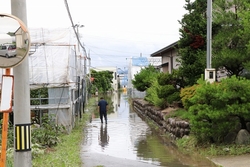 ビニールハウスと民家の間の道が浸水している写真