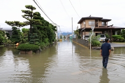 道路が浸水しており膝下まで水の中に浸かって歩いてる人の写真