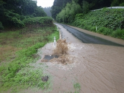 山中の道路でマンホールから噴き出したた泥水が流れ出ている写真