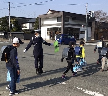 横断歩道を渡る小学生たちと旗を持って横断の誘導をする交通安全指導員の写真