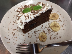 皿の上にチョコケーキの上に生クリームとミントがのっていてバナナを散らしてある写真