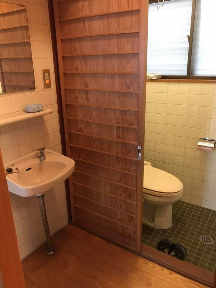 左側に洗面台があり、右側に半開きの扉と洋式トイレが見える部屋の写真