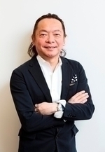 白い背景に黒いスーツ姿の安藤哲也さんが腕を組んで立っている写真