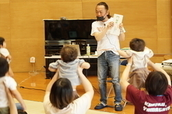 立っている白い服姿の安藤哲也さんに向けて赤ちゃんを掲げている親子たちの写真